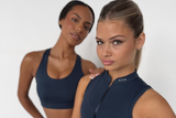 Two women wearing navy athletic outfits with a visible brand logo on a white background