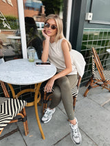 Woman sitting at an outdoor cafe table, wearing sunglasses and ATIA CHALLENGER TANK and CENTRED LEGGINGS.