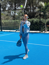 Person playing tennis on a blue court with trees in the background