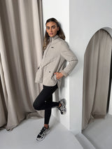Model leaving on the wall with leg up wearing the Versa 1/2 zip jacket in pebble