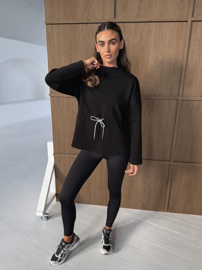 COMMENCE HOOD SWEATSHIRT in BLACK, worn with black leggings and trainers, featuring white drawcord waist detail