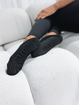 Black Pointe Ballerina Grip Socks worn on feet, showing textured grip sole detail on light furniture