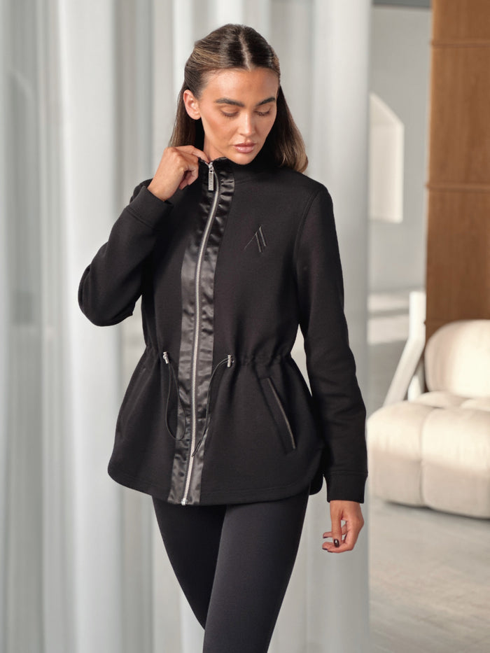 PREVAIL ZIP JACKET in BLACK, worn with drawcord waist and high neck, styled with black leggings