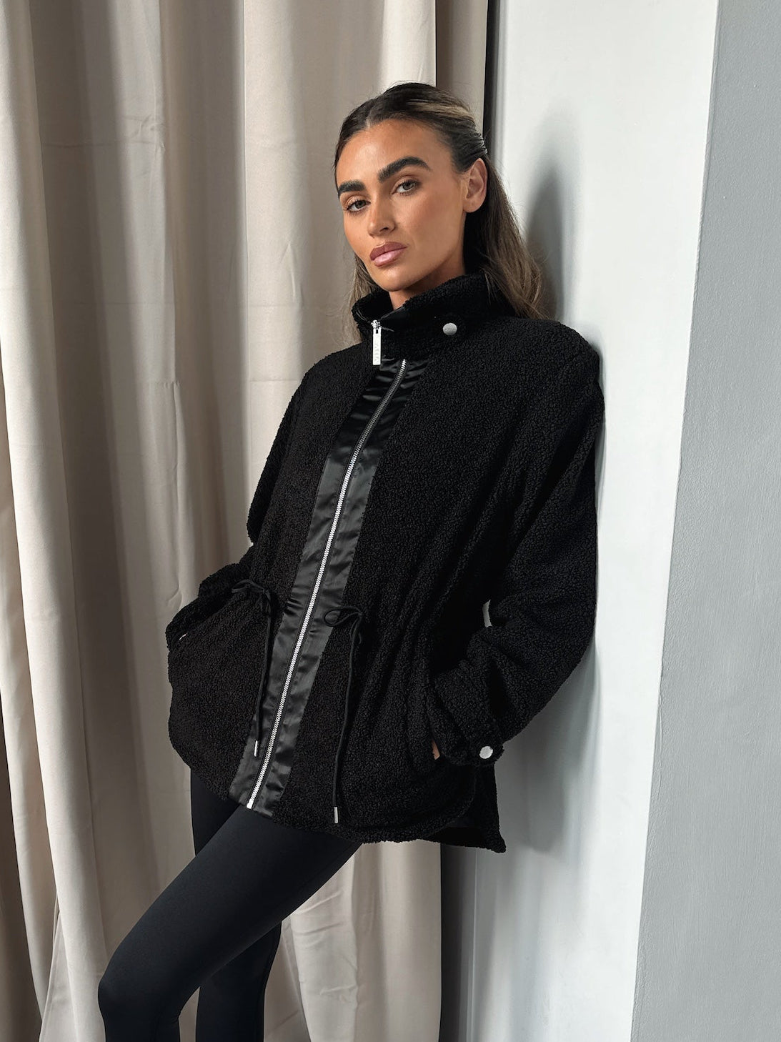 Woman in black Freedom Sherpa Jacket from Atia Active outfit leaning against a curtain
