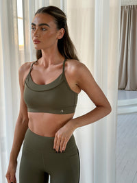 Centred Sports Bra in Olive Night, worn with matching leggings, front view on model in minimal interior setting