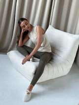 Model posed on a lounge chair wearing the CHALLENGER vest in a beige neutral tone and olive toned leggings